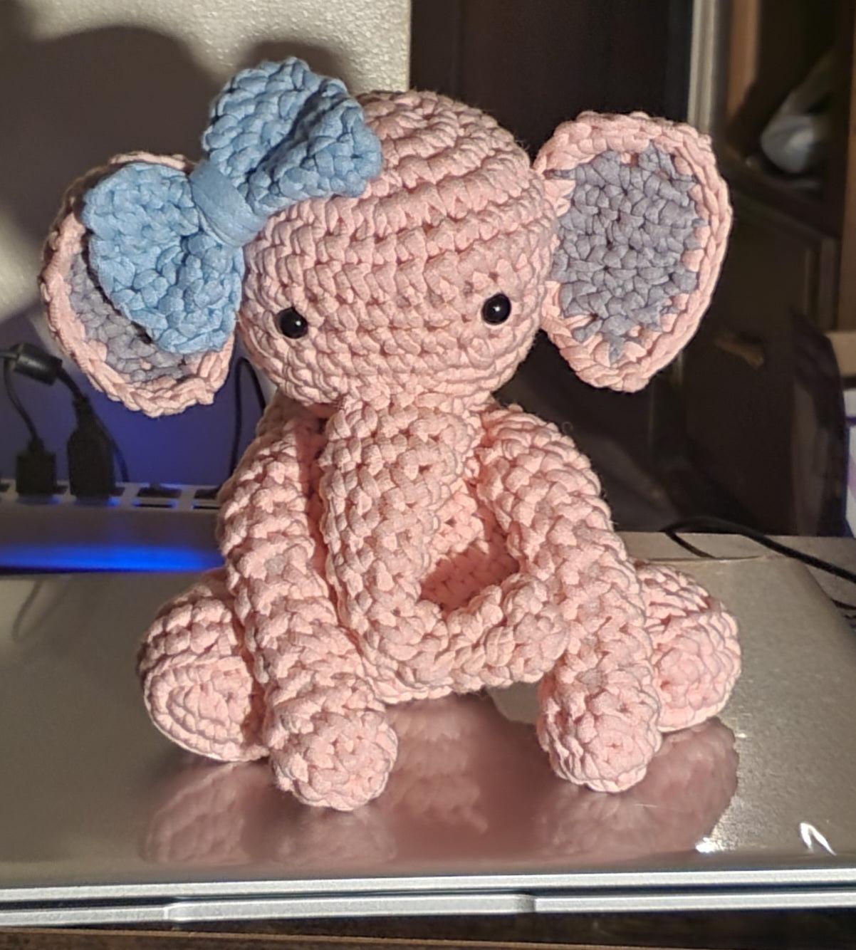 Pink crocheted stuffed elephant doll toy with blue bow with a blue bow, perfect for collecting and display in a child's room.