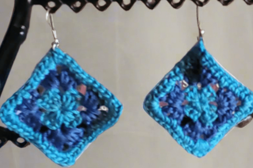 Crocheted granny square earrings in light and dark blue displayed on stand.