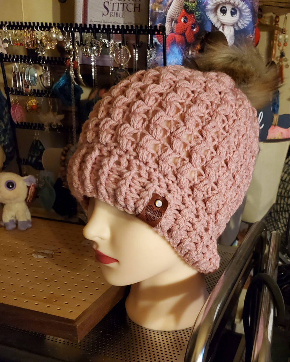 Mauve colored crocheted hat with pompom on display mannequin.