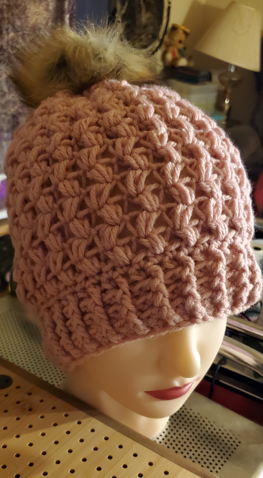 Mauve colored crocheted hat with pompom on display mannequin.