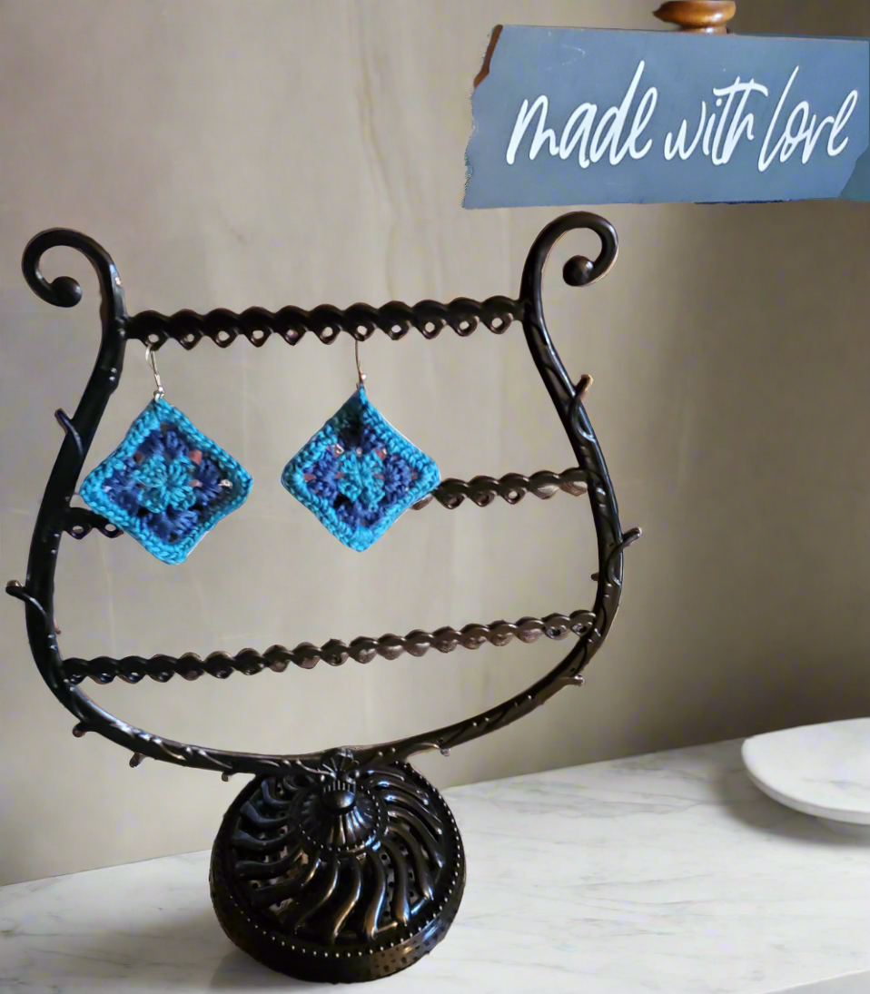 Crocheted granny square earrings in light and dark blue displayed on stand.