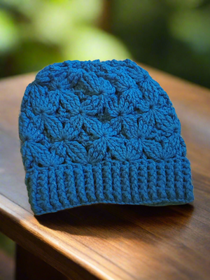 Beautifully crocheted flower of life hat for women on wooden surface, teal color.