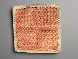 Crocheted cream and tangerine dishcloth with intricate stitching.