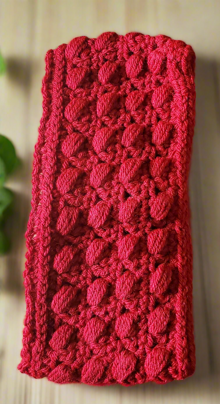 Beautifully crocheted red puff stitch ear warmer headband on display with natural elements.