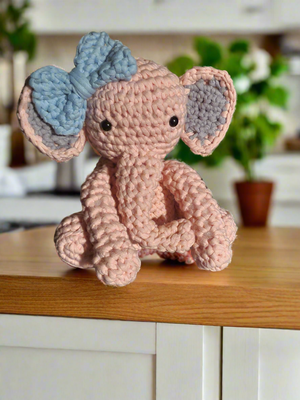 Pink crocheted stuffed elephant doll toy with blue bow, handmade for playtime or collecting.