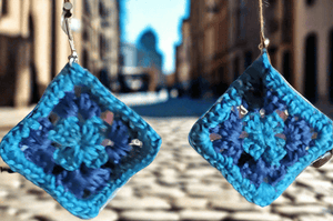 Crocheted granny square earrings in light and dark blue hanging outdoors.