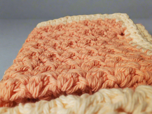 Set of four crocheted cream and tangerine dishcloths, showcasing soft and absorbent texture.