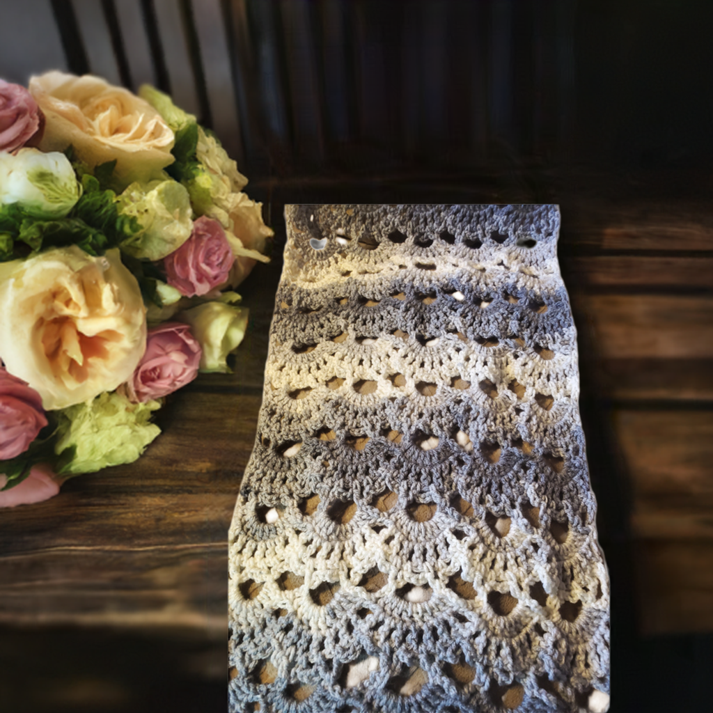 Gray and white crocheted handmade scarf on wooden table with bouquet.