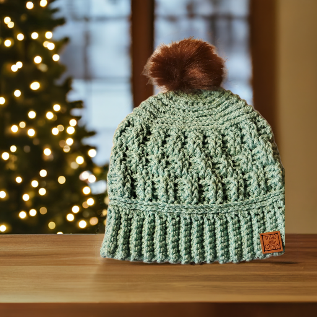 Handmade crocheted aqua winter hat with pompom for women on wooden table.