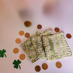 Handmade green and white crocheted dishcloths on white background with decorative coins and shamrocks.