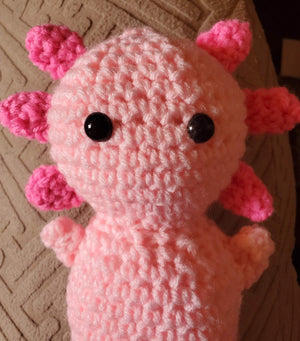 Adorable handmade crocheted pink axolotl toy with black eyes, perfect for collections.