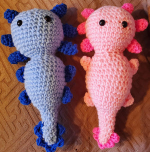 Adorable handmade crocheted stuffed axolotl toys in blue and pink.